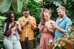 Four adults using smartphones surrounded by lush greenery in an outdoor setting, enjoying technology in nature.
